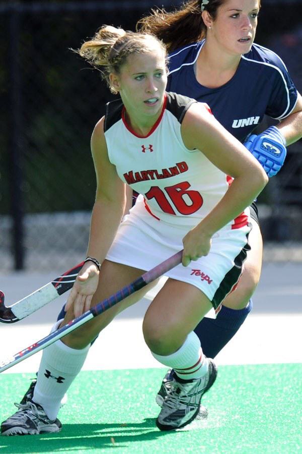 Female field hockey player holding stick on green turf