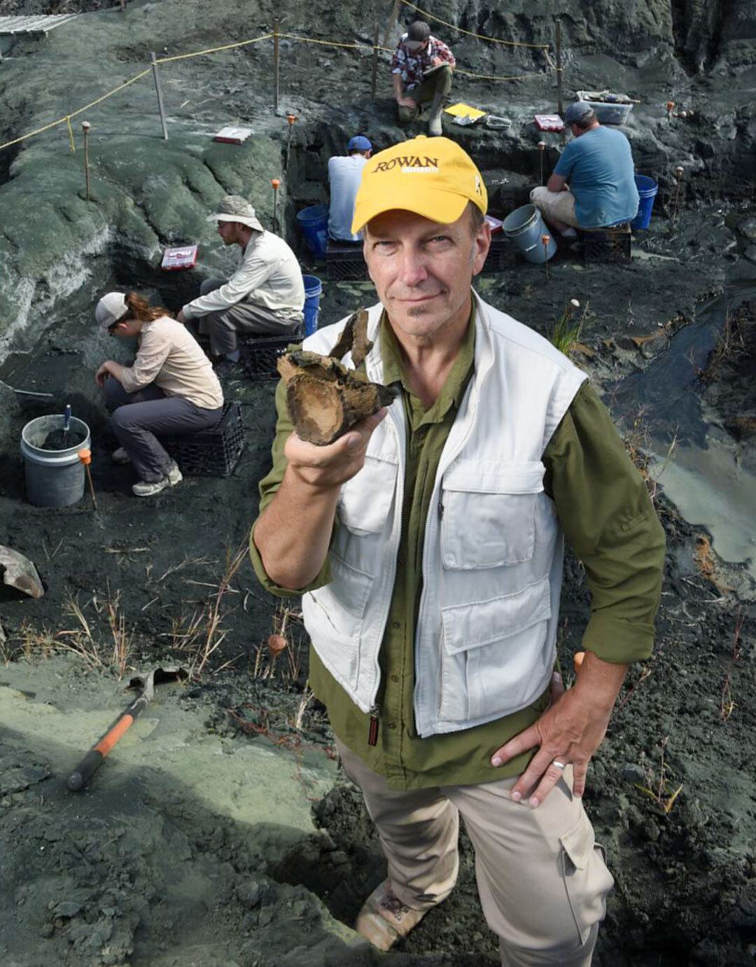 Kenneth Lacovara holds fossil as people dig behind him