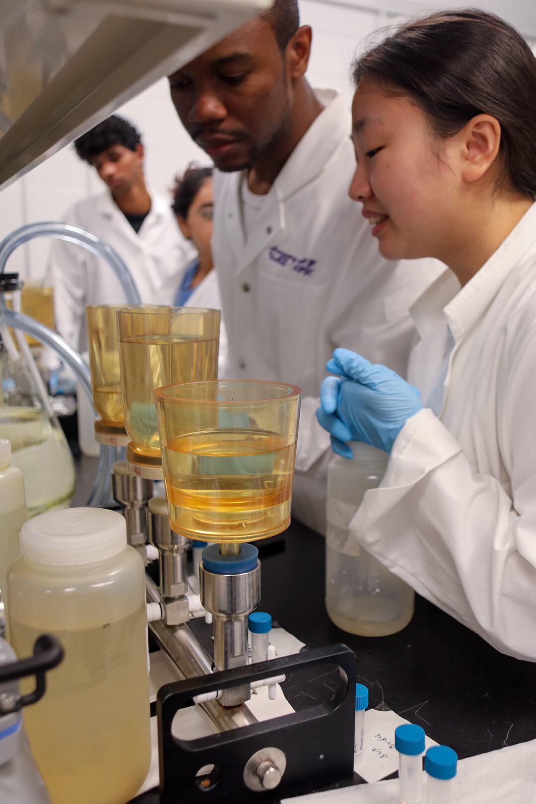 students in lab coats filter water samples