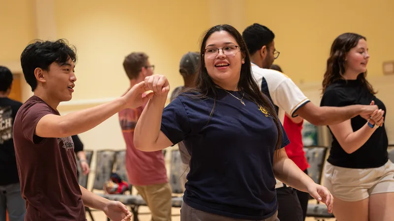 A male and female student hold hands and dance