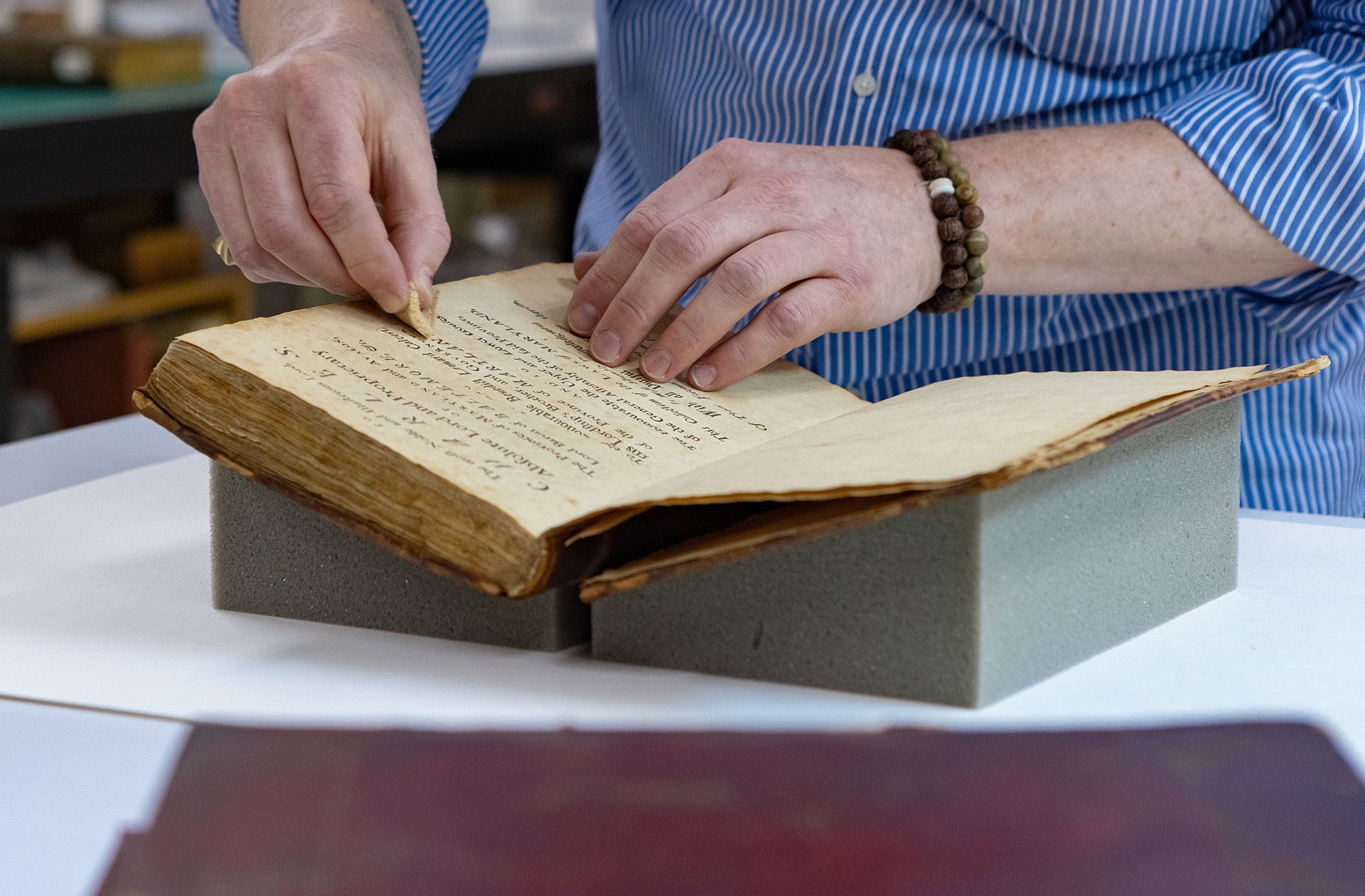 A hand holding a small sponge wipes off an old book