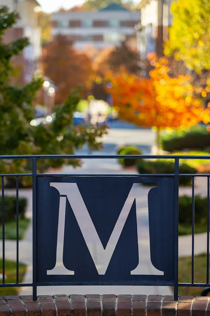 M in iron gate with fall foliage in background