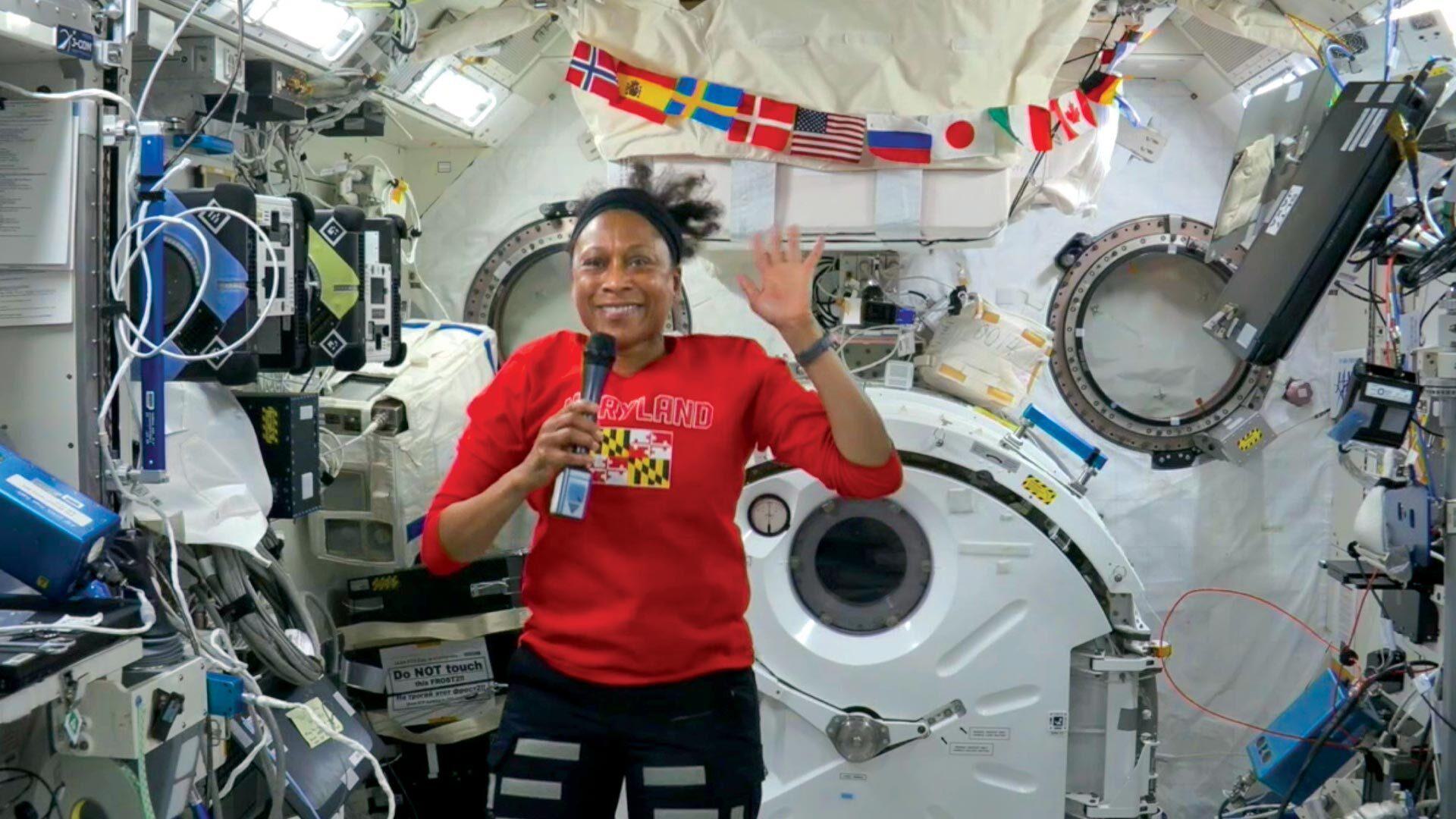 Jeanette Epps floats and waves aboard ISS while wearing red Maryland shirt