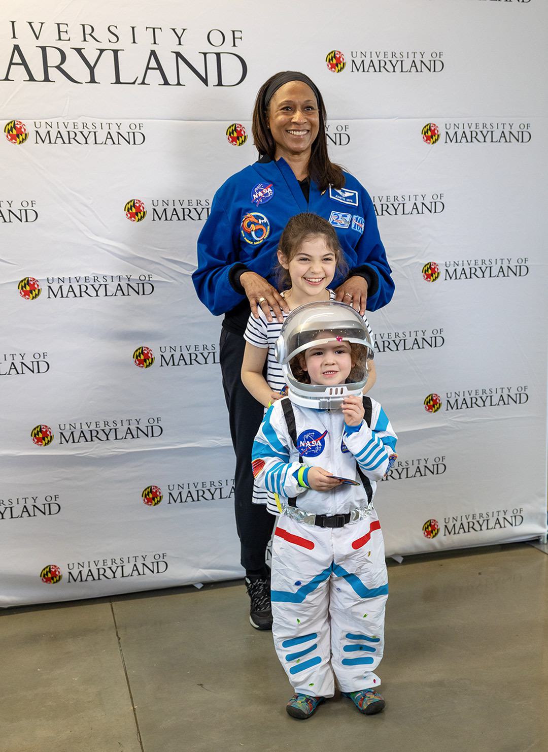 Woman stands with two children in front of her, one wearing a space suit costume