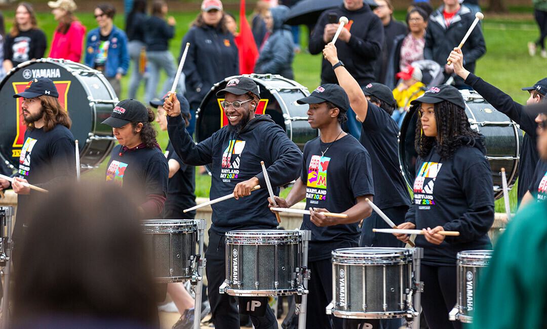 several students in a drumline play while smiling