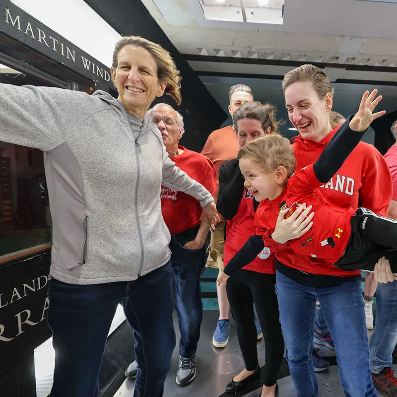 A group of people smile and spread their arms, including a kid being held, in a wind tunnel