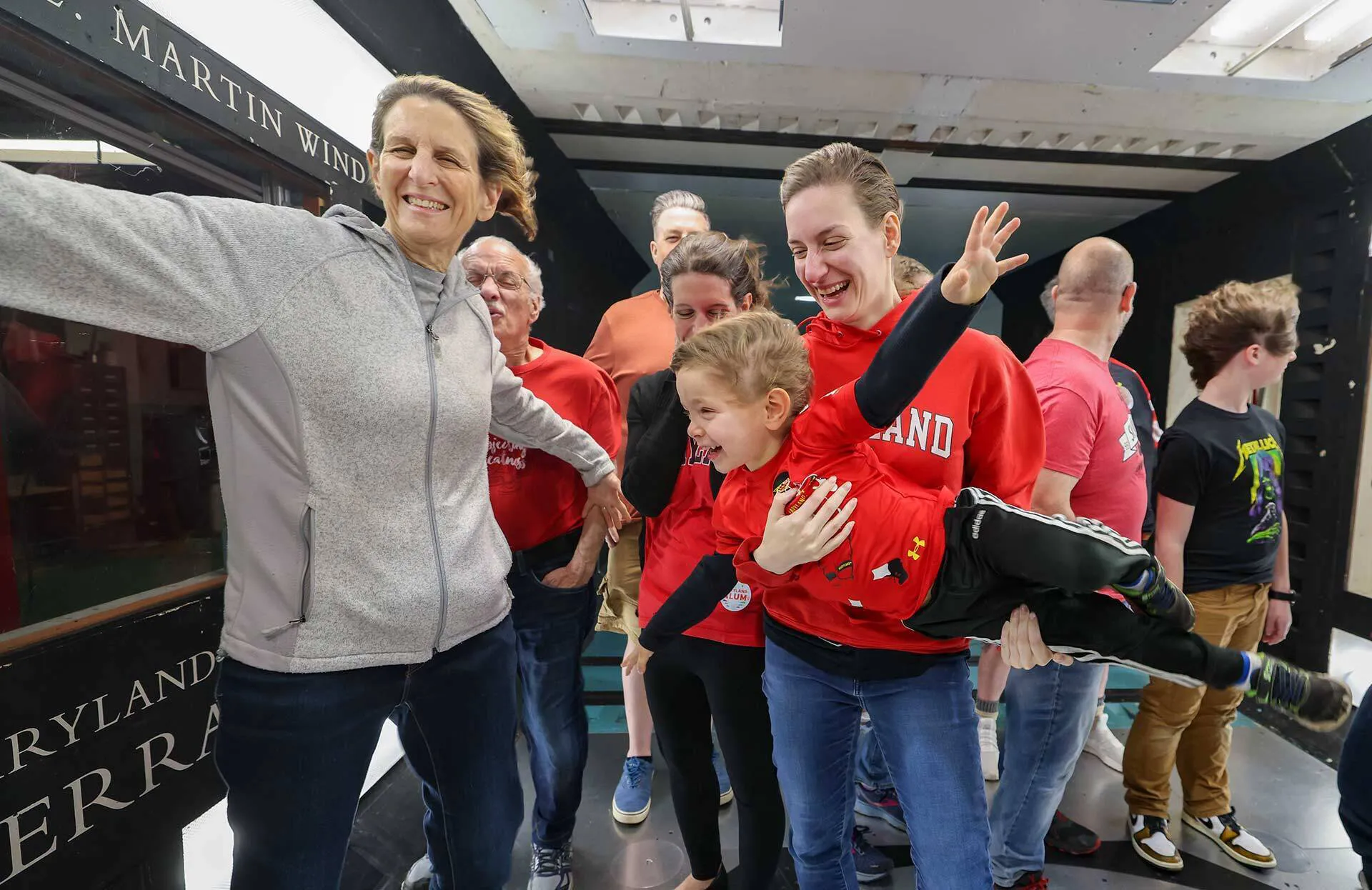 An adult holds a child with his arms spread in a crowd inside a wind tunnel