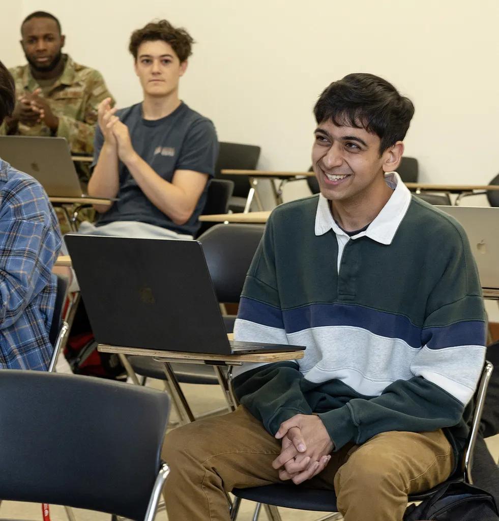 Dhruvak Mirani smiles at his desk as other students clap