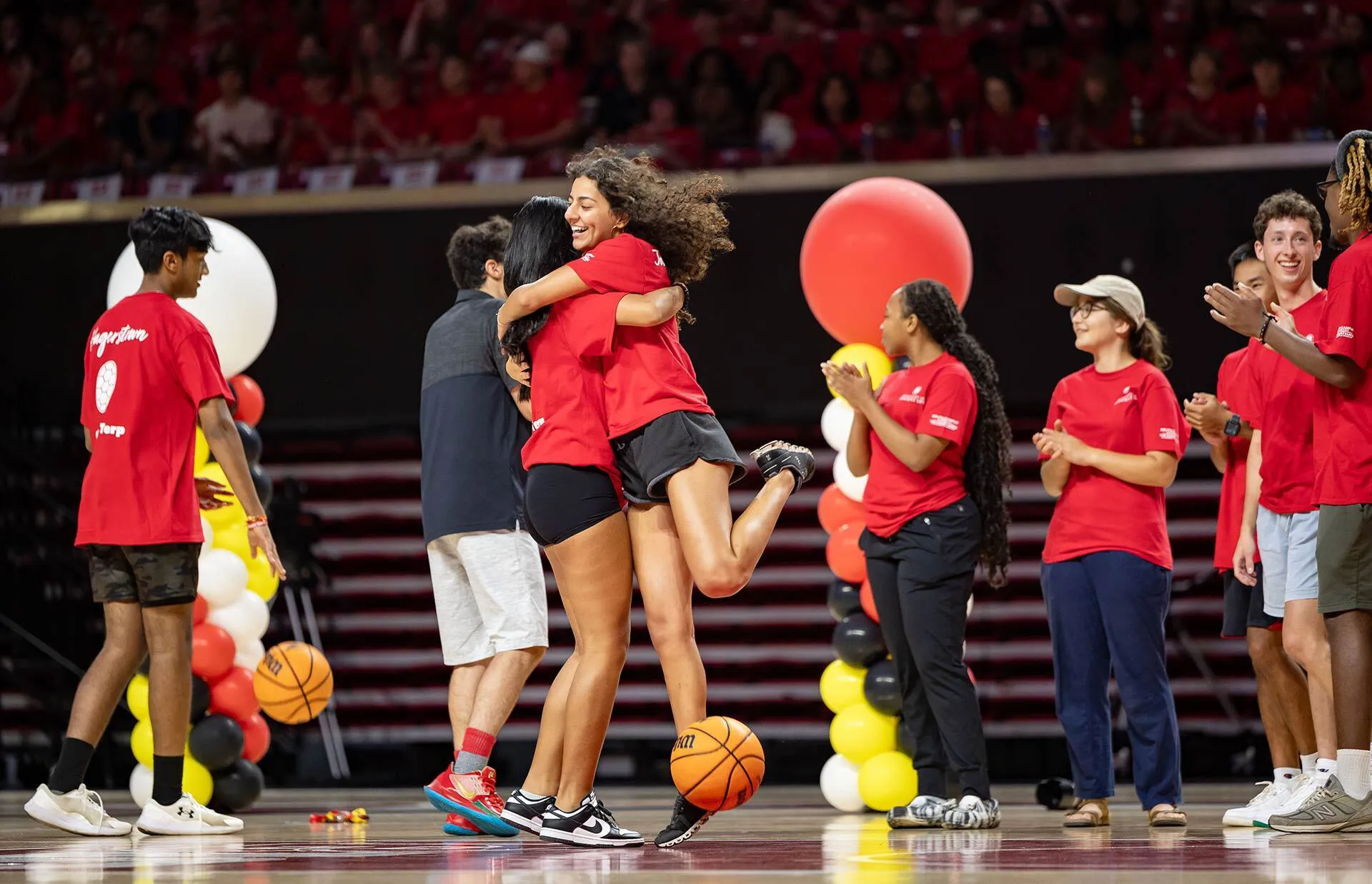two female students joyously hug on basketball court