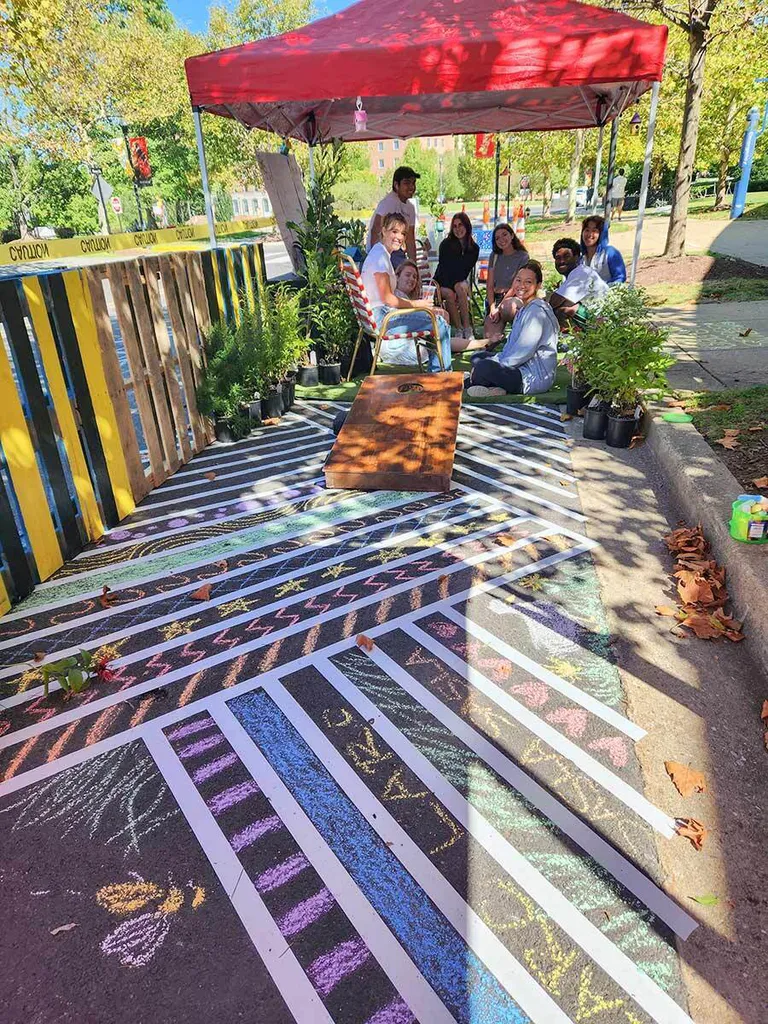 group sits under tent with cornhole board in chalk-decorated parking space