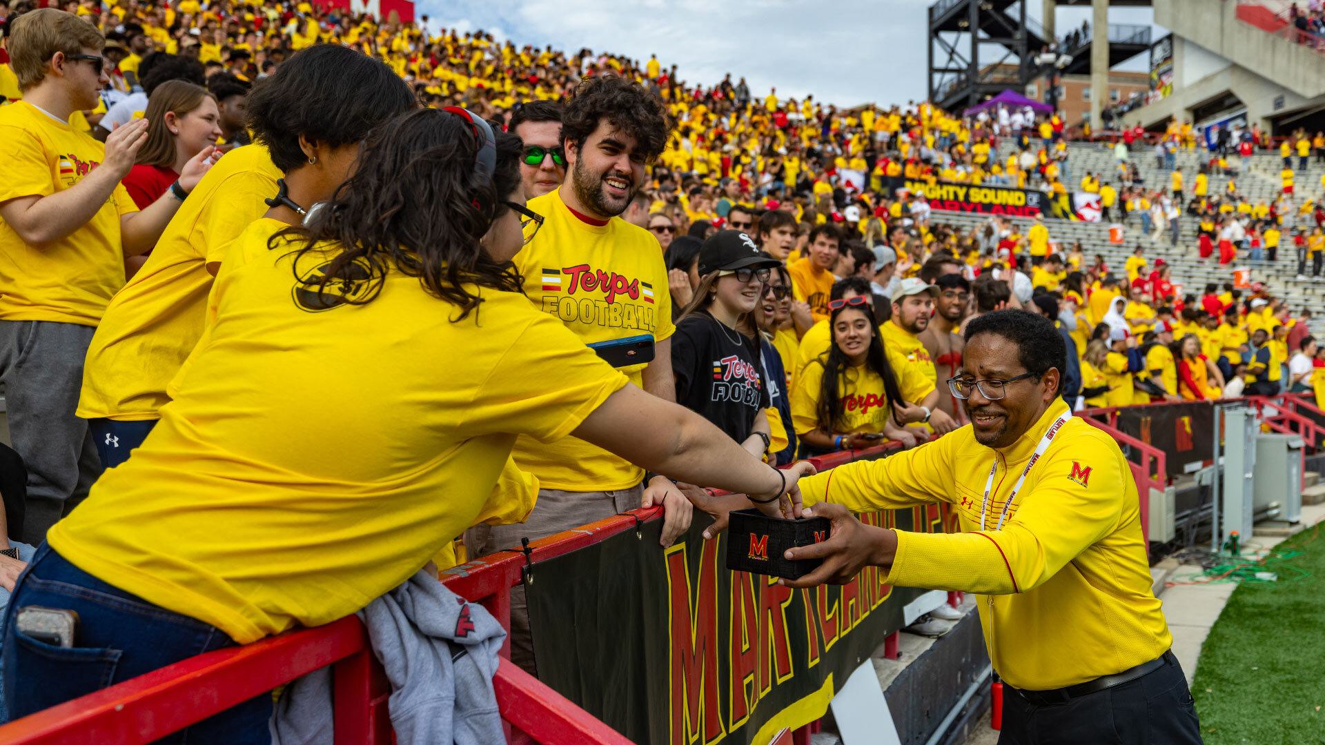 President Pines hands out turtle pins to students in the stands at a football game