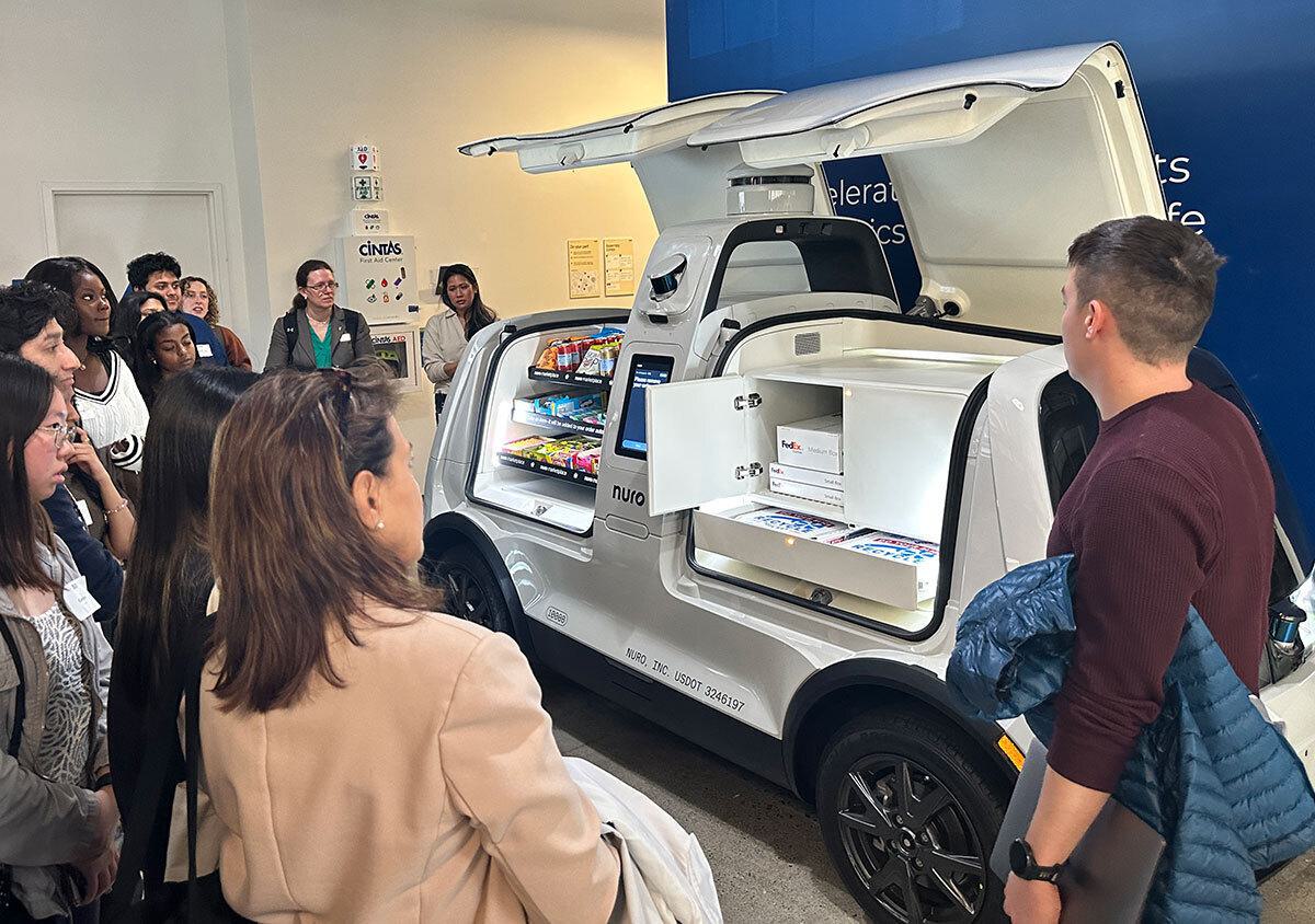 Students look at Nuro's white delivery vehicle with butterfly wings open, showing snack products inside