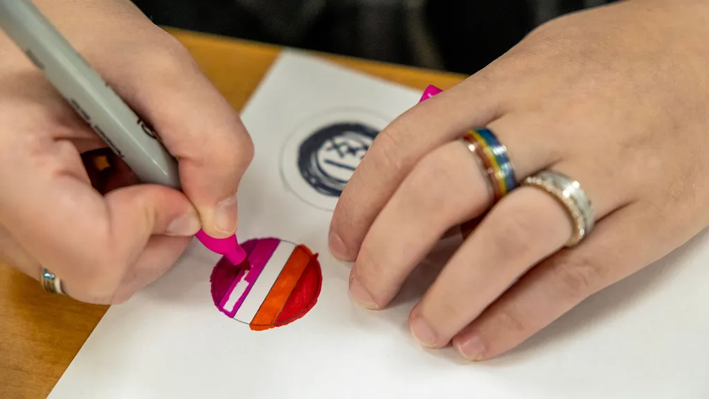 close-up of hand wearing a rainbow ring coloring in a pink and orange circle
