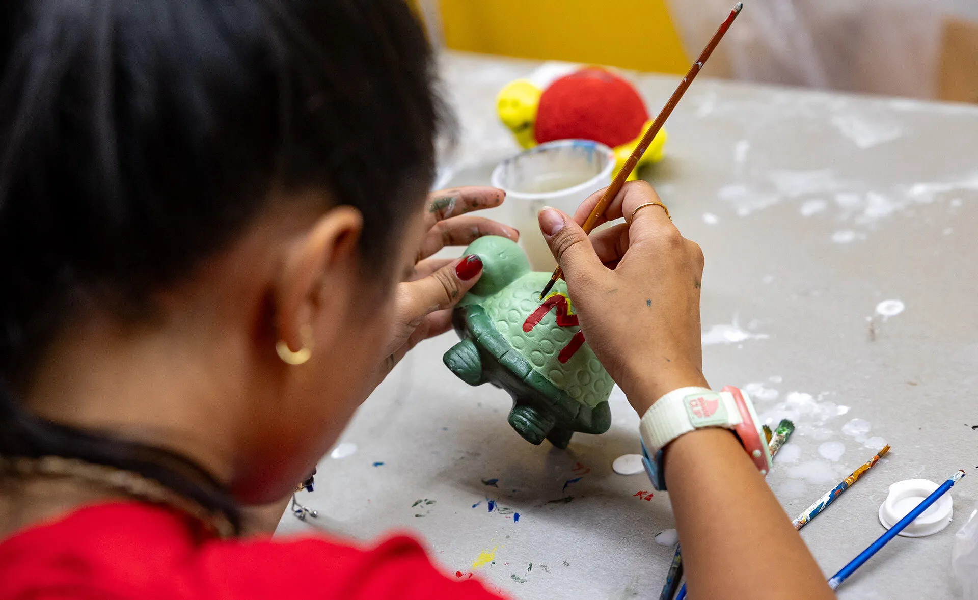 A young woman paints a green cerarmic looking turtle