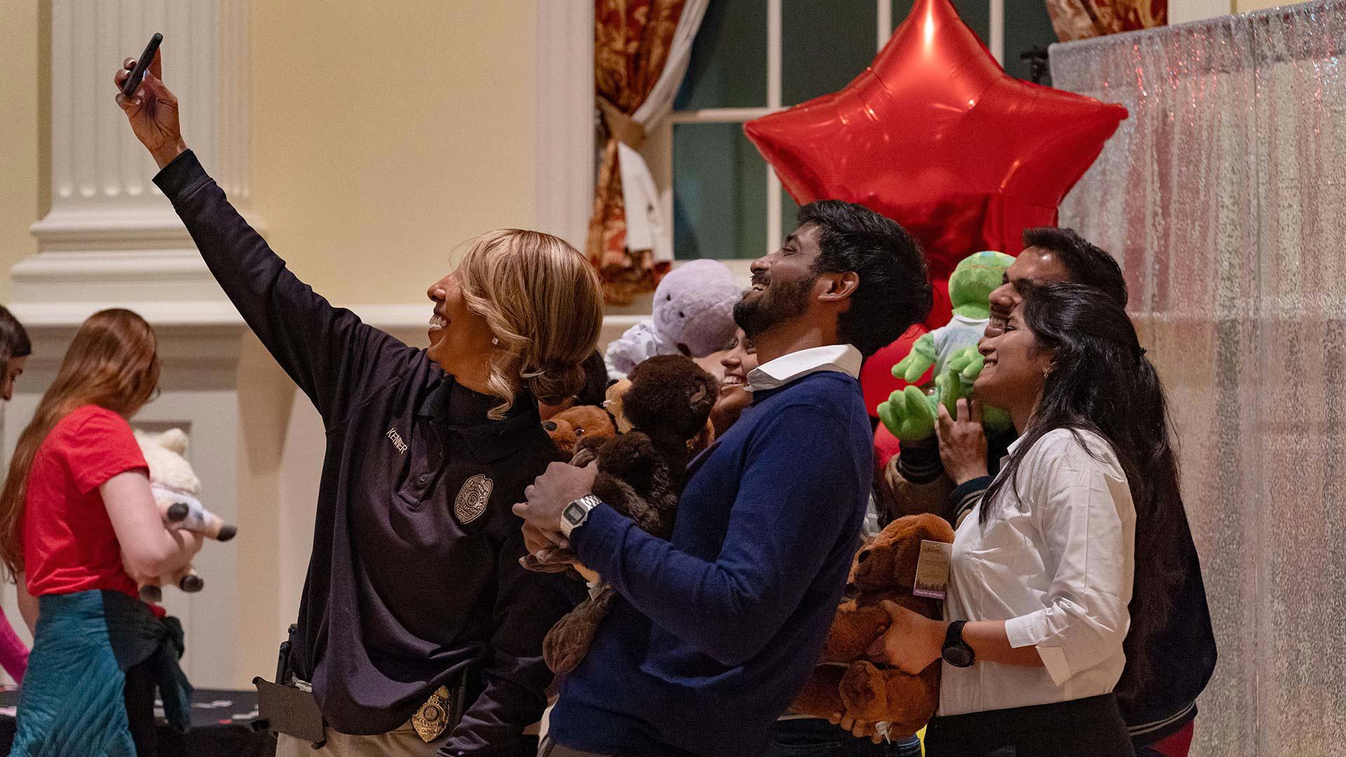 A UMPD officer takes a selfie with several people holding stuffed animals