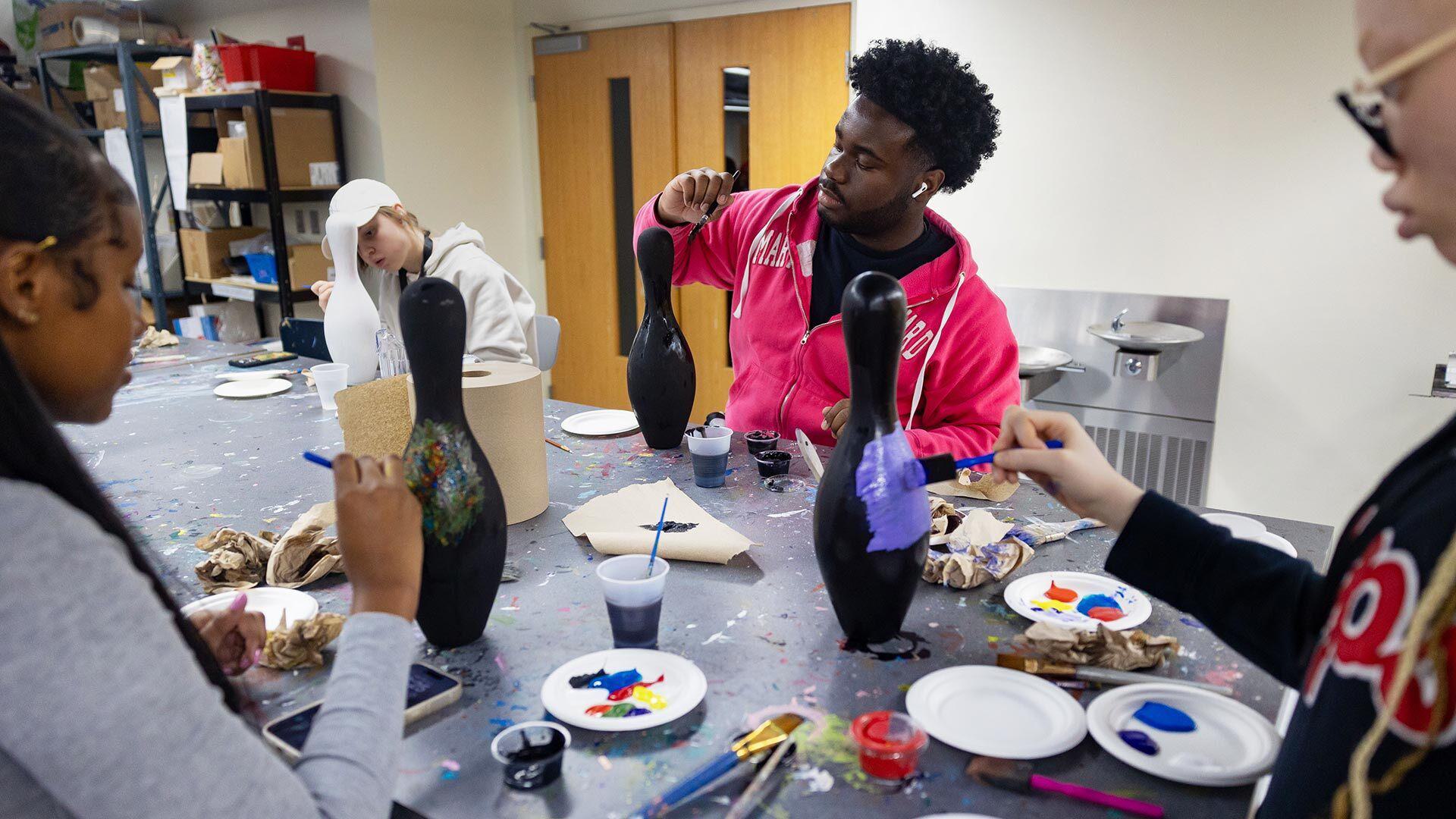 People decorate bowling pins at a table