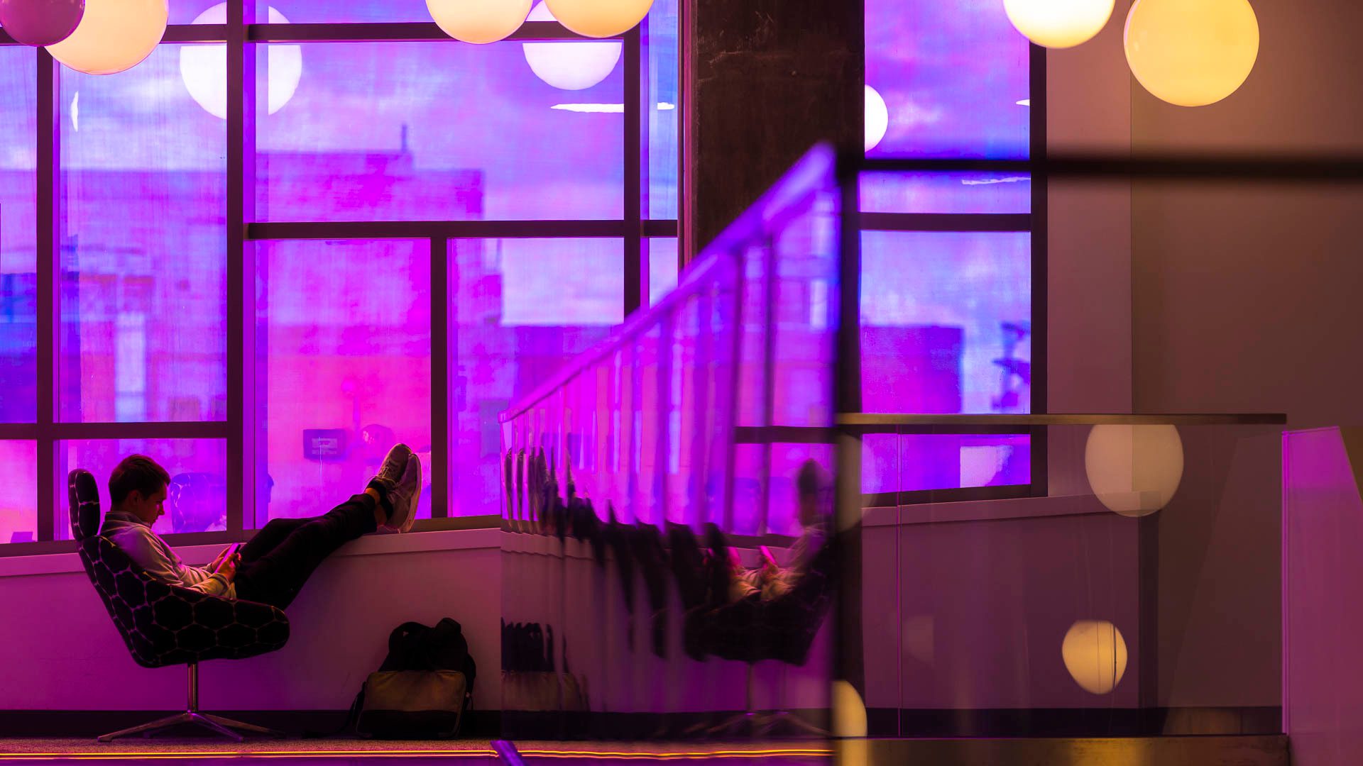 student sits with feet up, with purple/pink windows