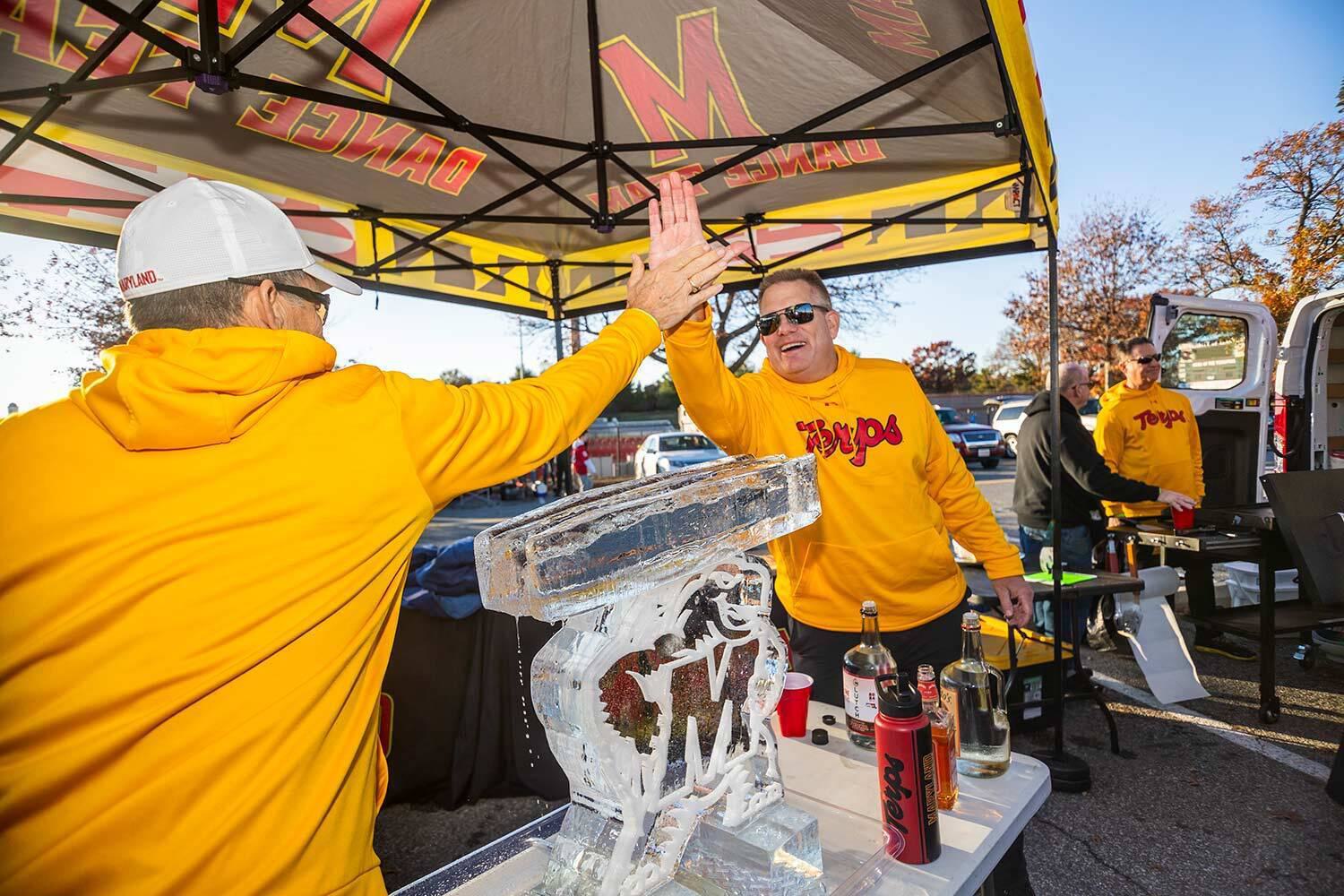 two tailgaters in gold sweatshirts high-five next to Testudo ice luge