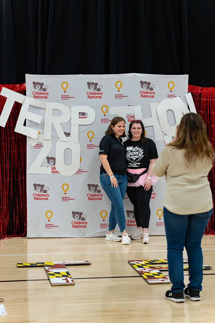 two women pose for a photo in front of a placard