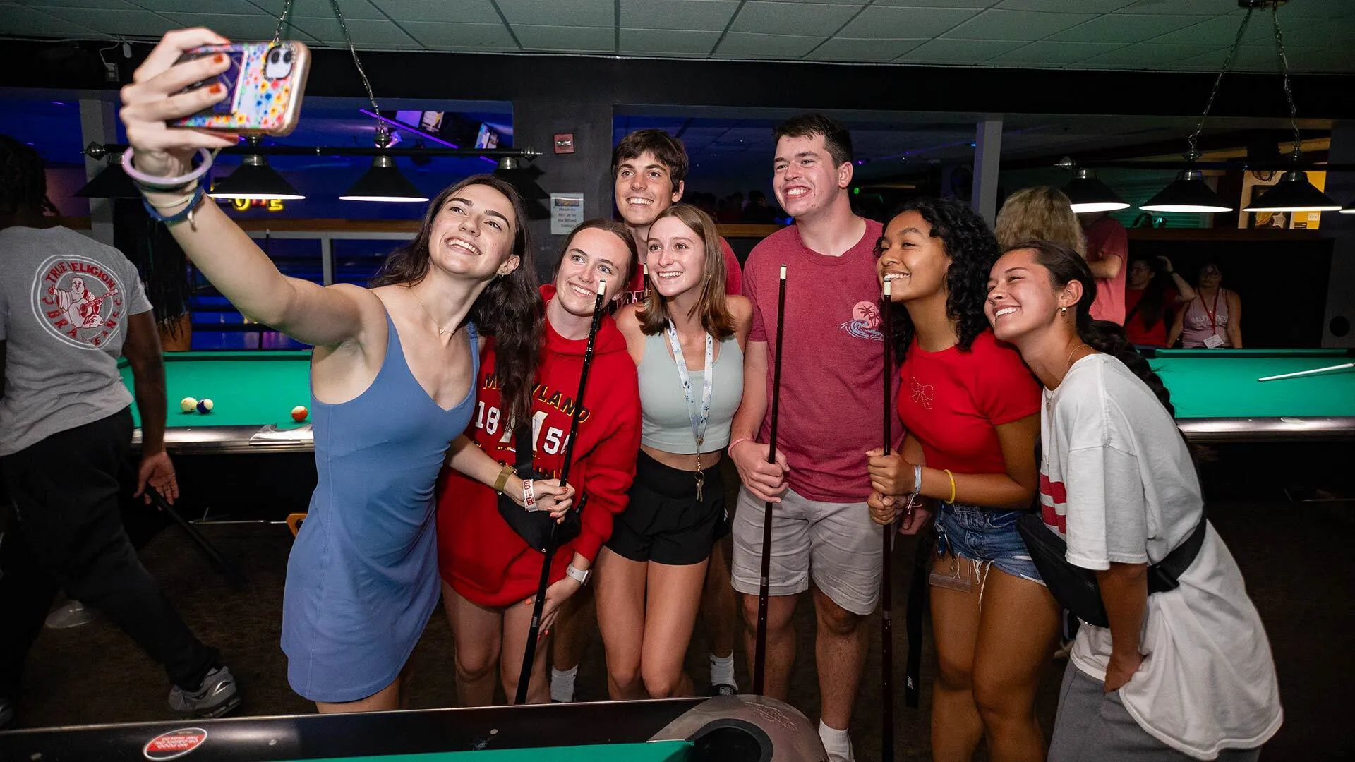 seven smiling young people in a billiards hall pose for a selfie