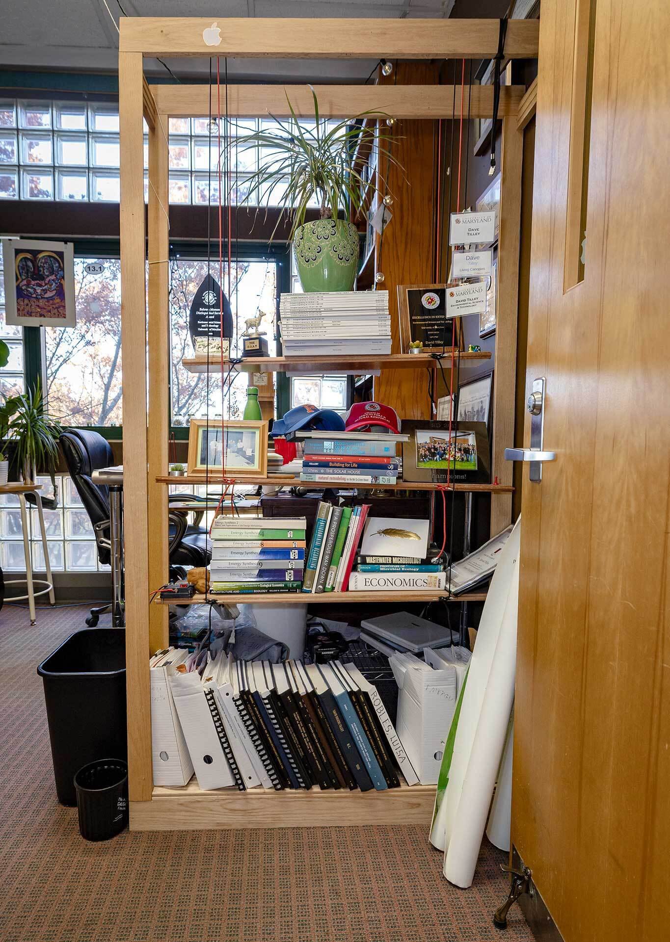 A homemade bookshelf with swinging shelves, filled with books, plants and knicknacks