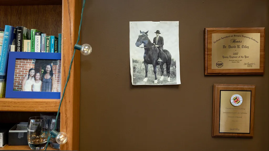black and white photo of a man in a hat sitting on top of a horse taped to a brown wall, surrounded by awards