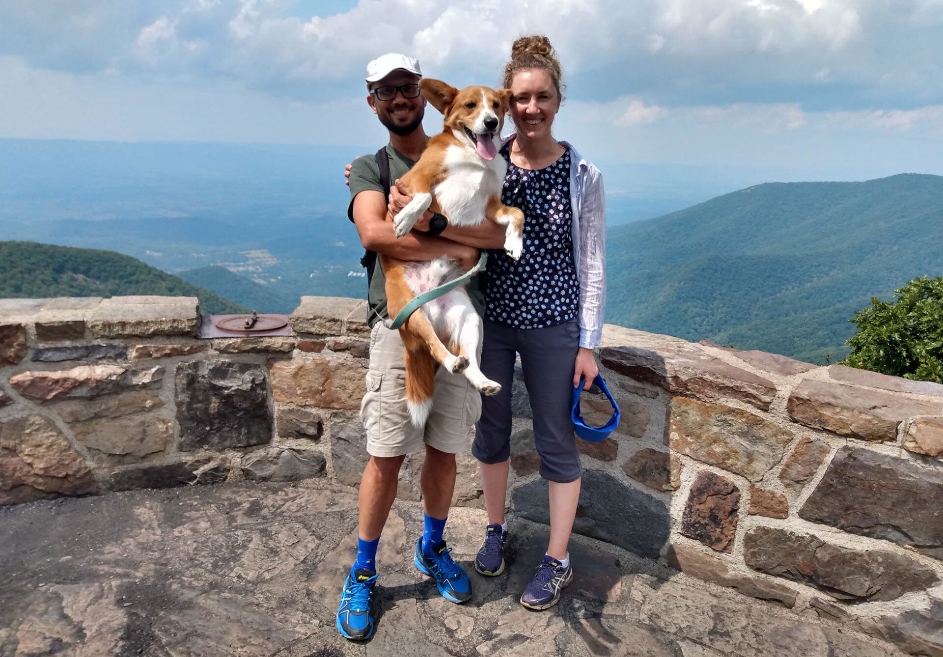 couple holds dog near ledge with mountains in background