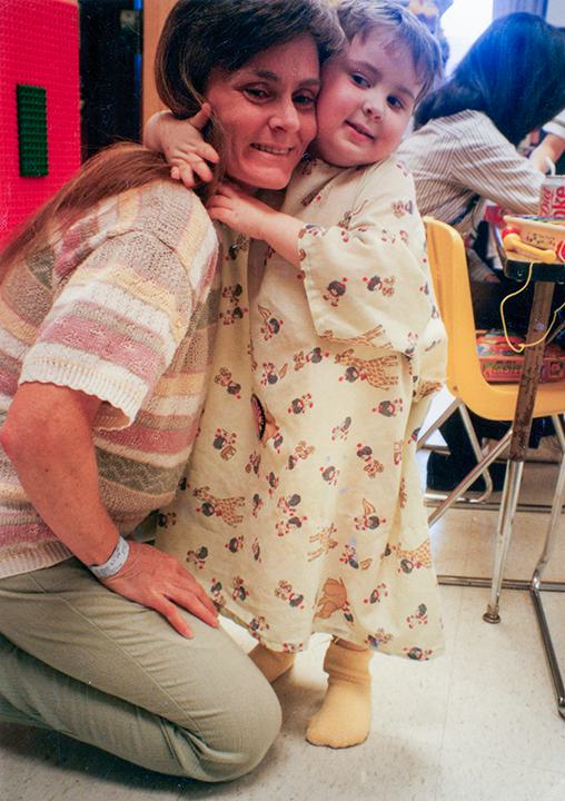 Young boy in hospital gown hugs kneeling woman.