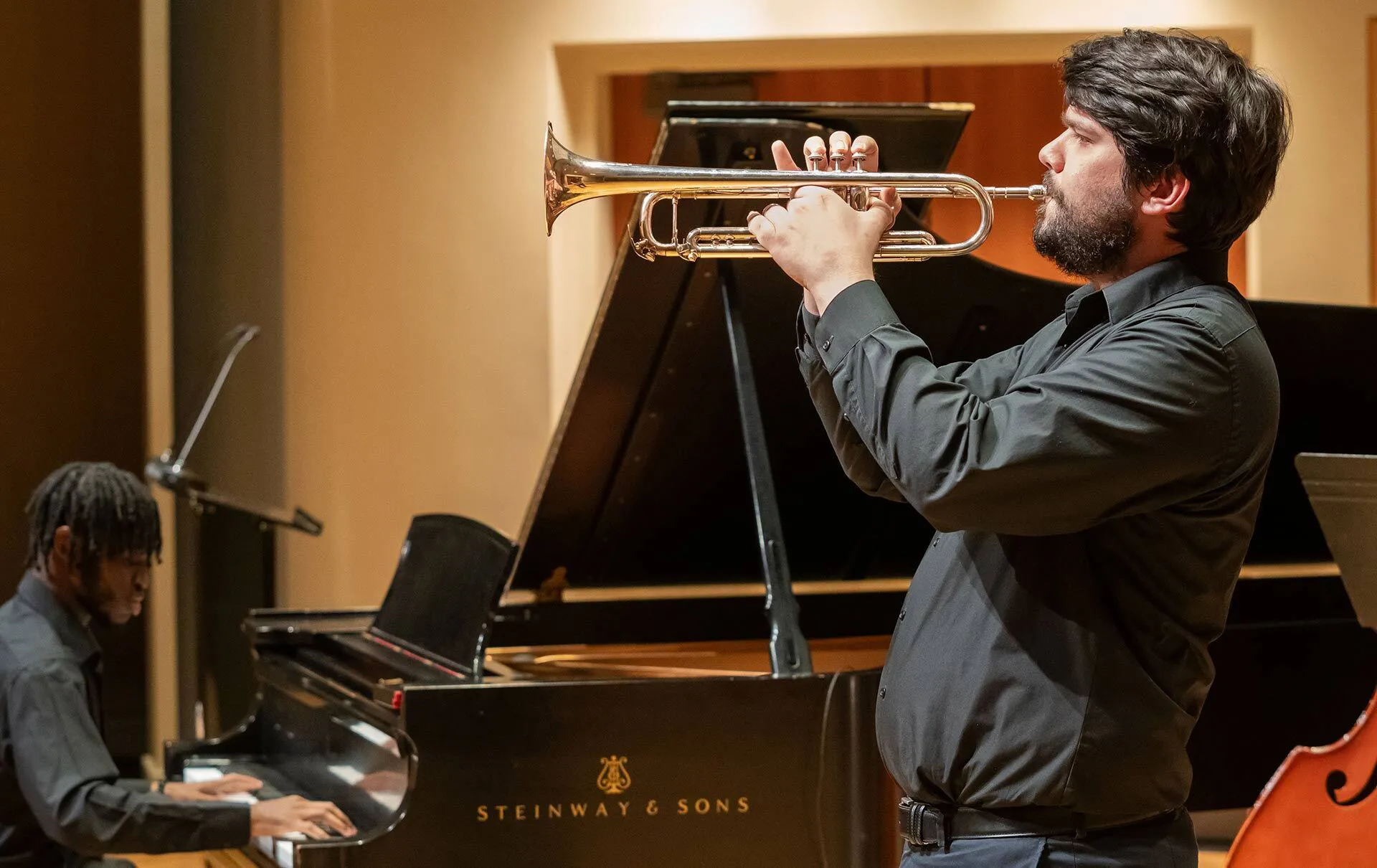 a man plays a trumpet with a man playing piano behind him