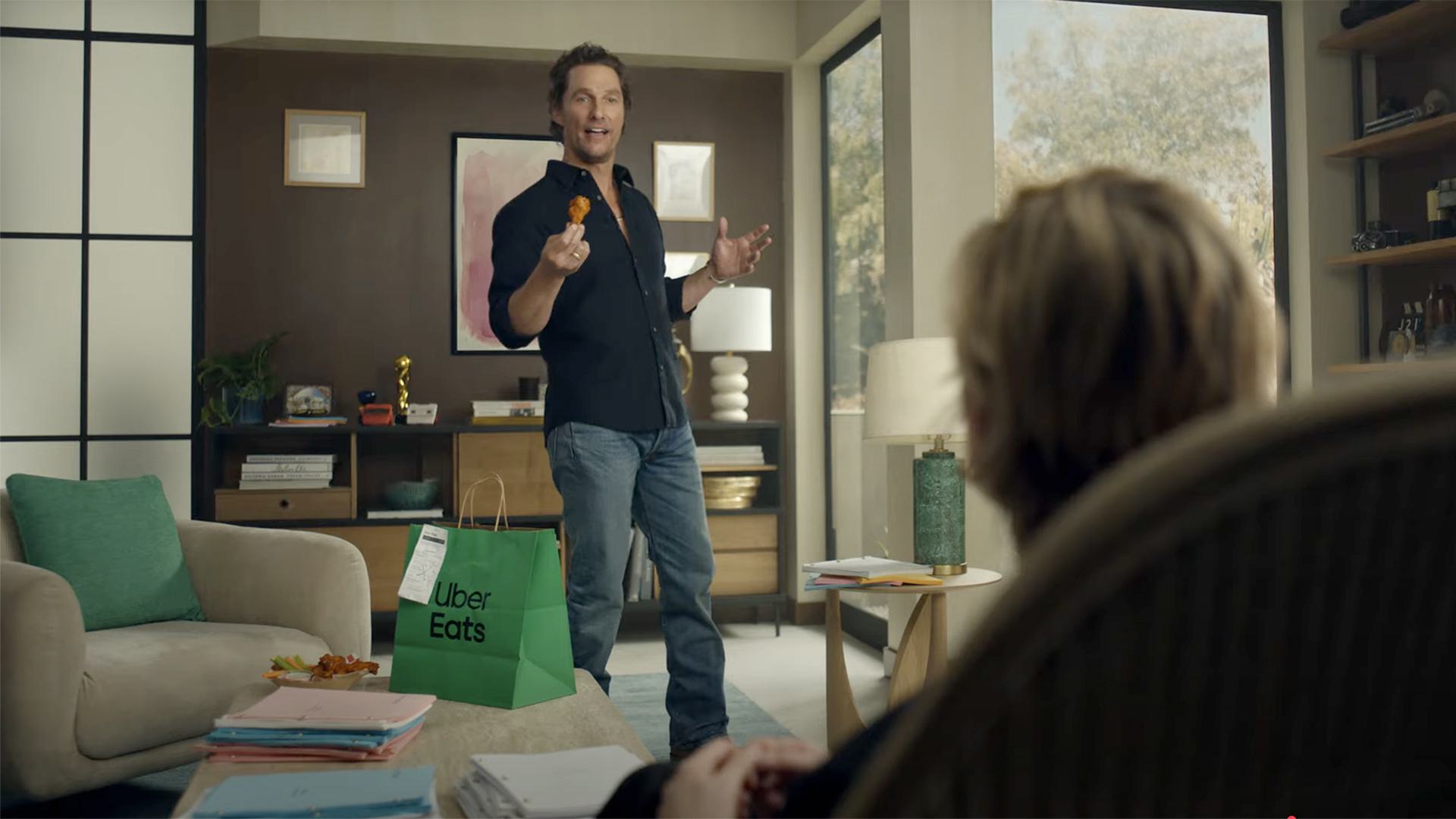 Matthew McConaughey talks while holding chicken wing, with green Uber Eats bag