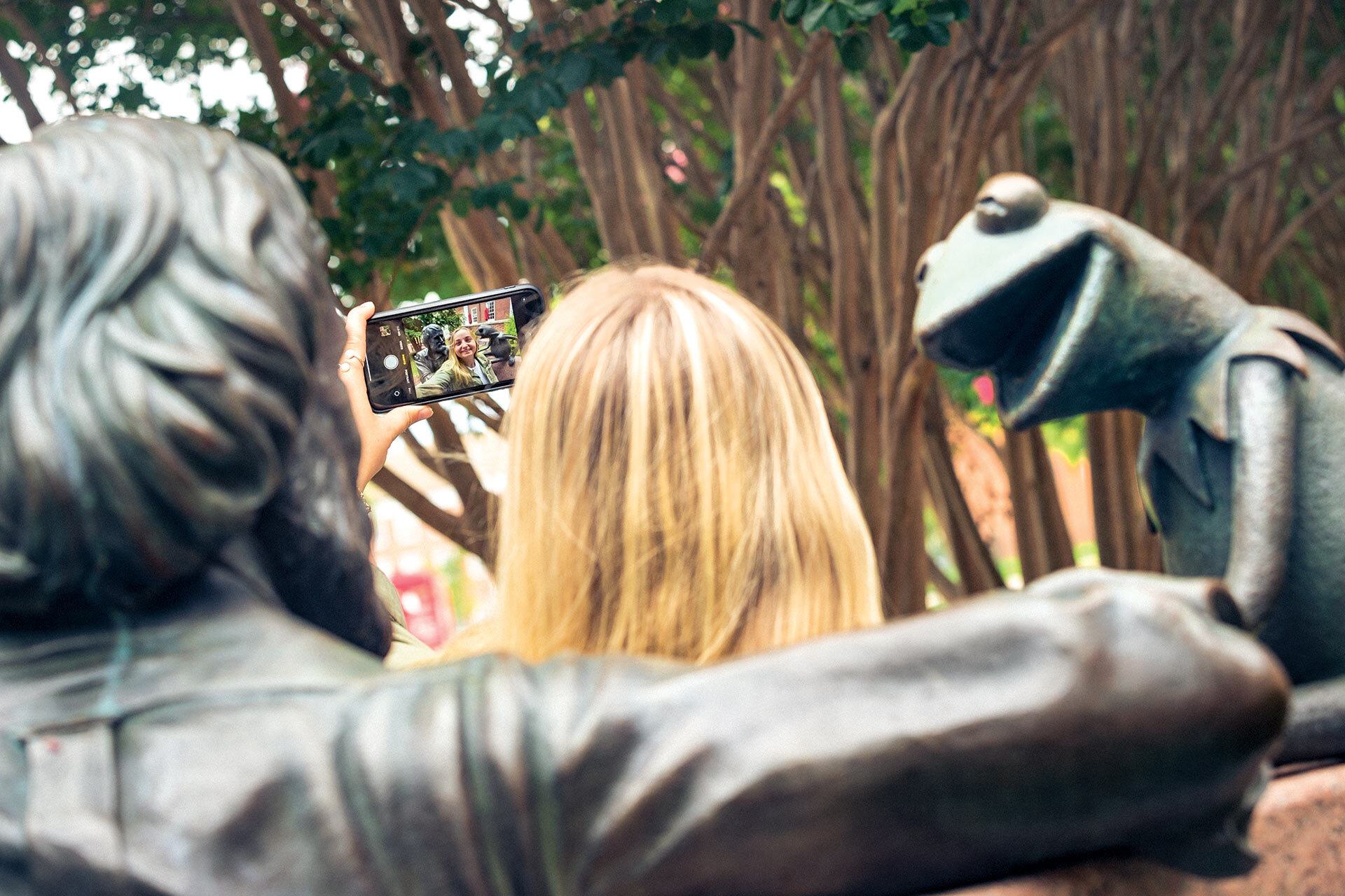 student takes a selfie at Jim Henson statue