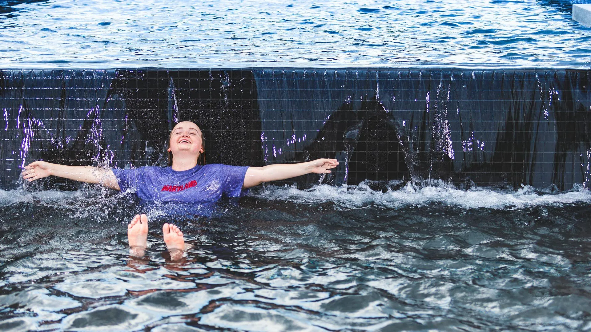 student sitting in ODK fountain holds out arms as water falls on her