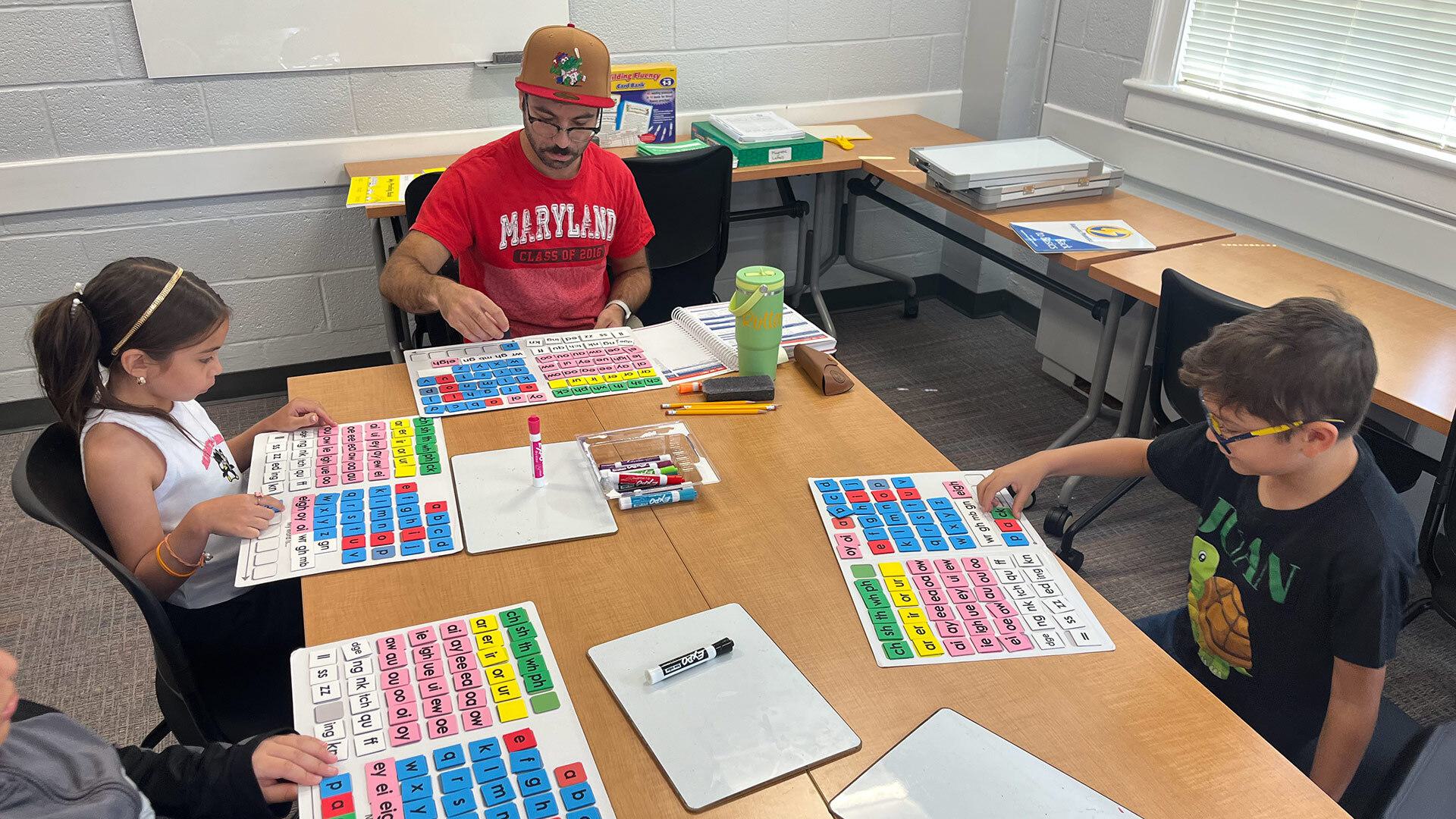 A man in a Maryland shirt teaches students phonics on a board