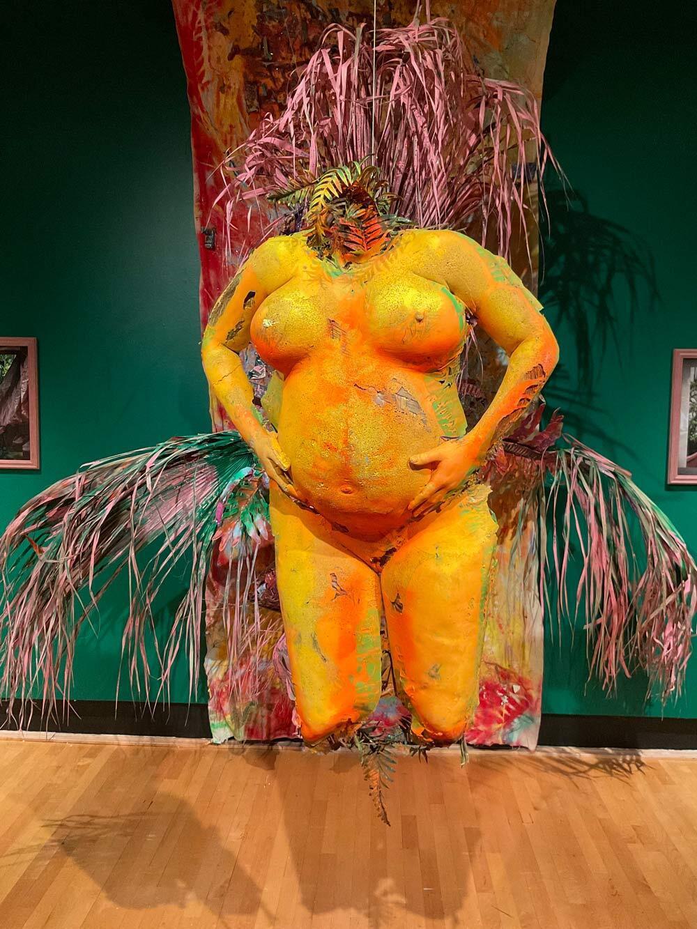 Orange sculpture of headless, footless woman holding her stomach