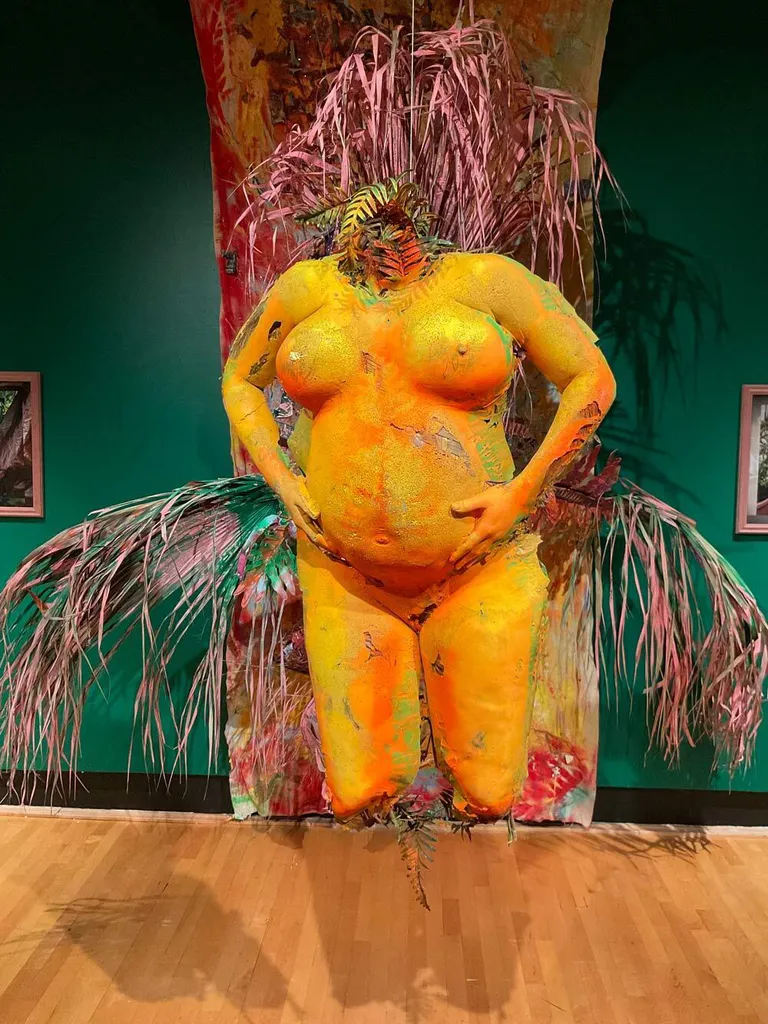 Orange sculpture of headless, footless woman holding her stomach