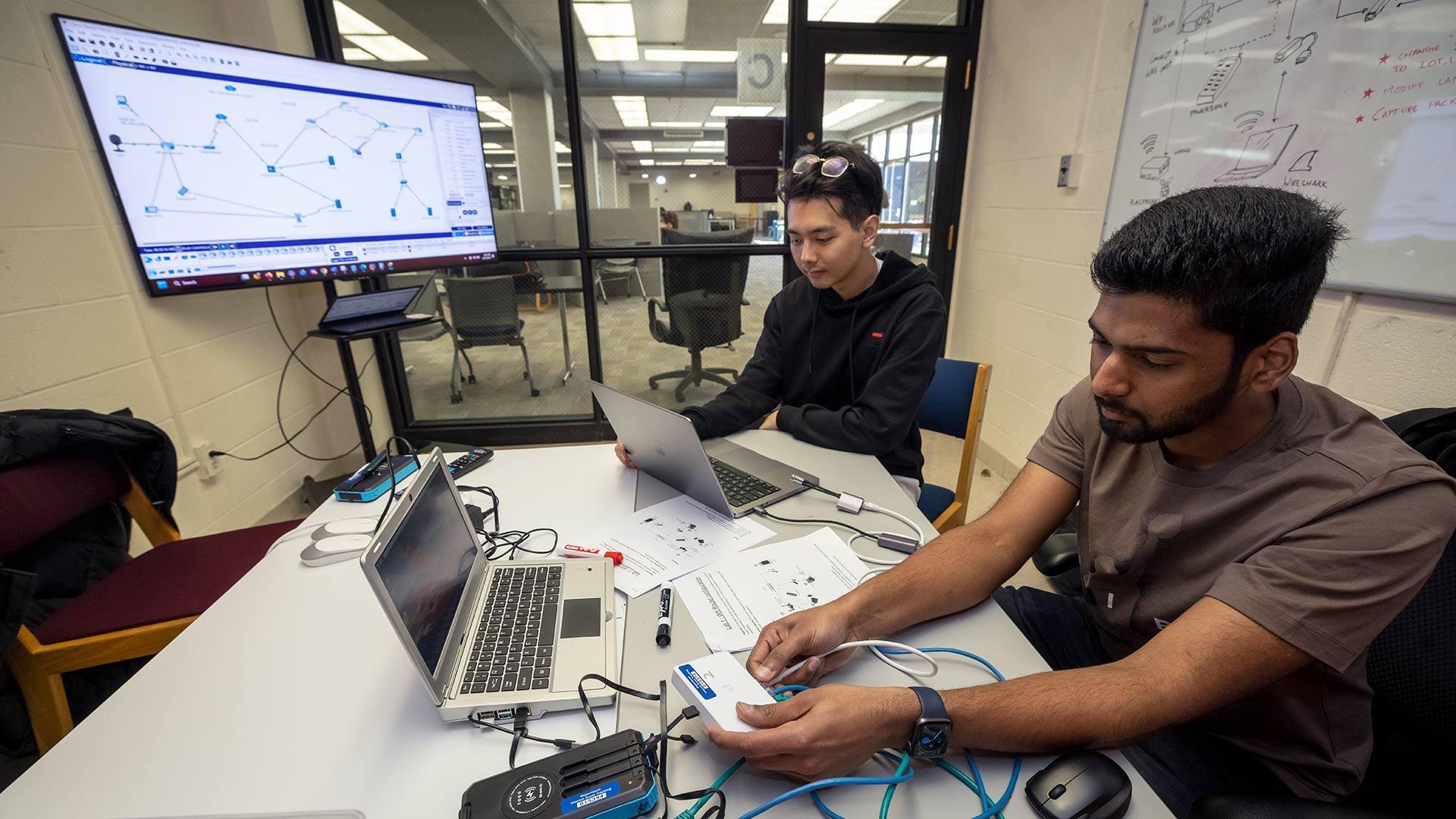 two students work on laptops in study space