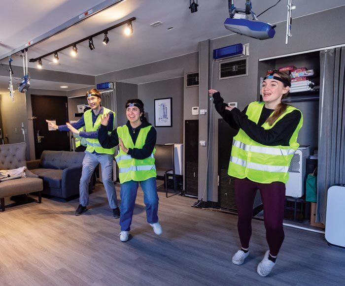three people wearing bright yellow vests play dancing video game