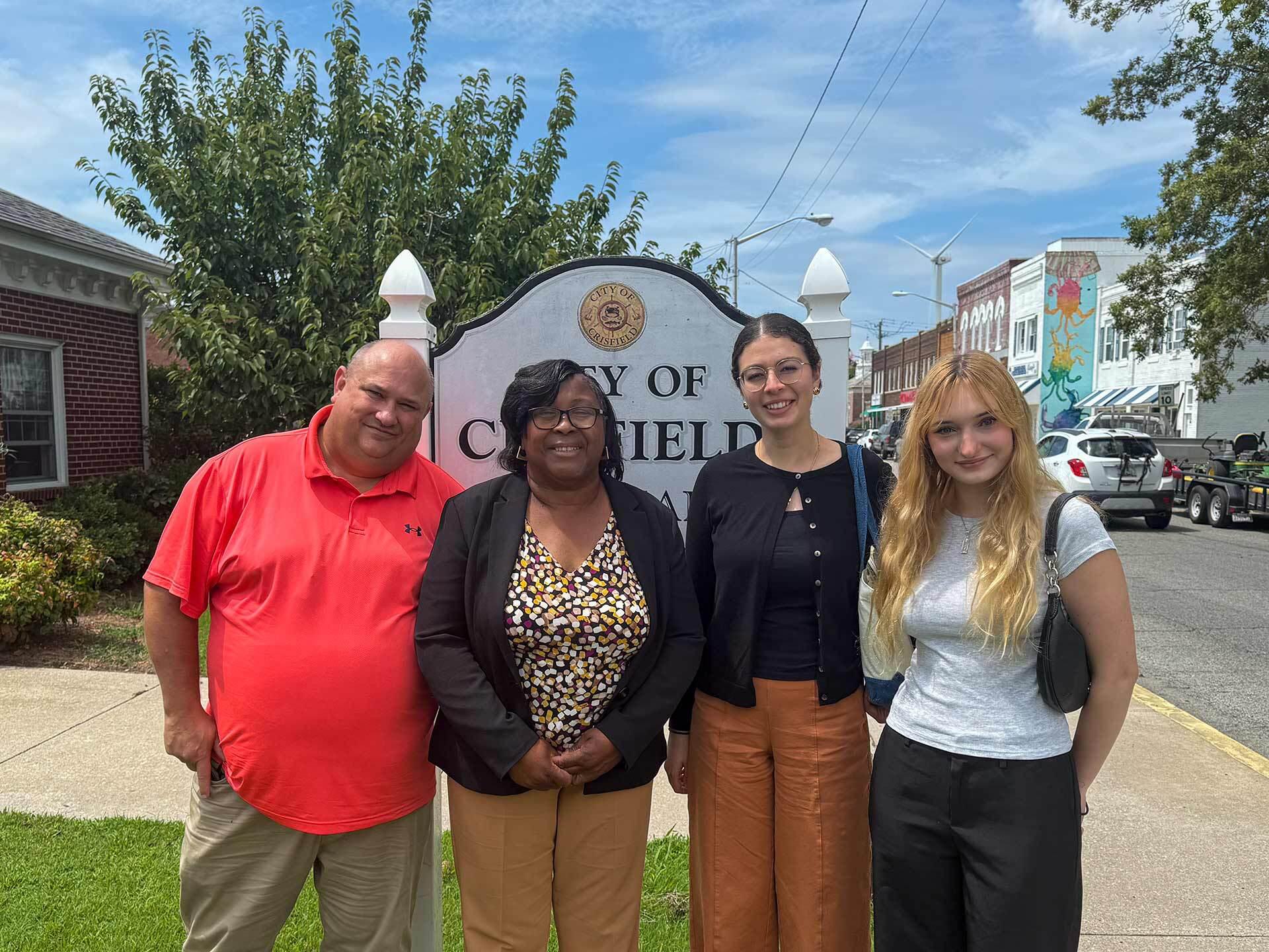 group of four poses in front of City of Crisfield sign