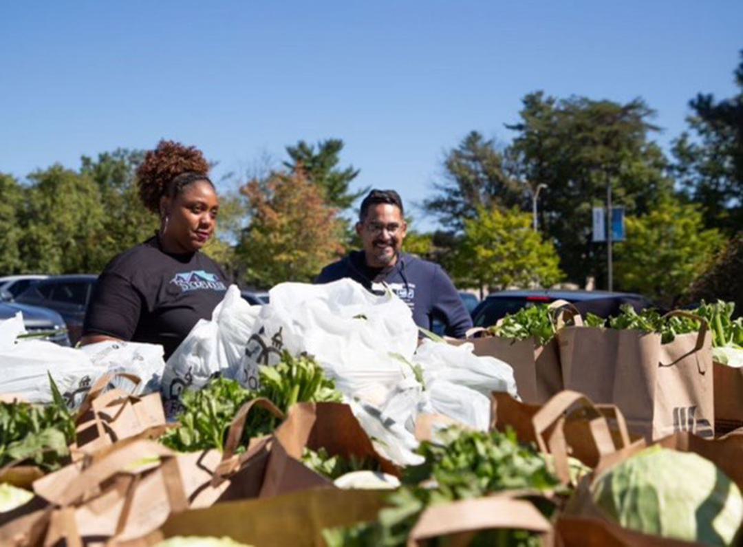 two volunteers with grocery bags of greens