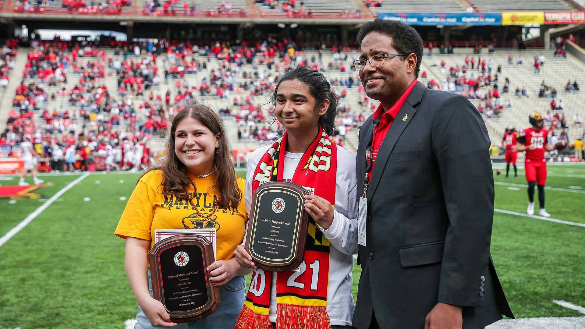 Spirit of Maryland Award winners Josie Shaffer, left and M. Pease are honored on Capital One Field with President Darryll J. Pines.