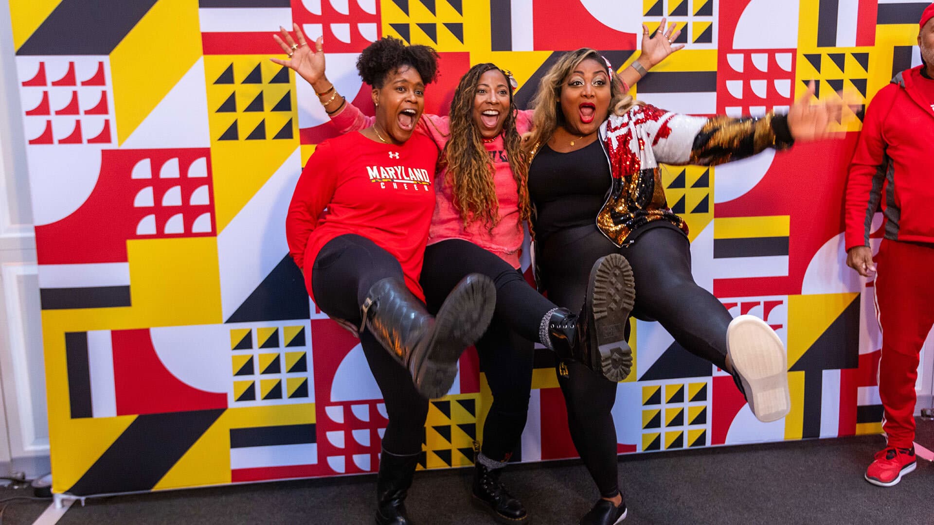 three people kick festively for the camera in front of a photo backdrop