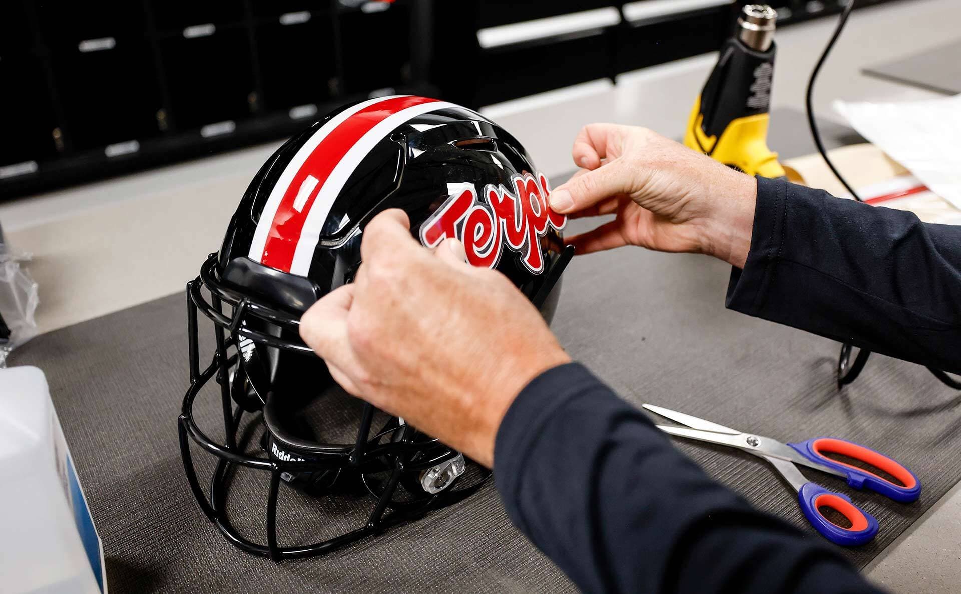 closeup of hands putting Script Terps sticker on football helmet