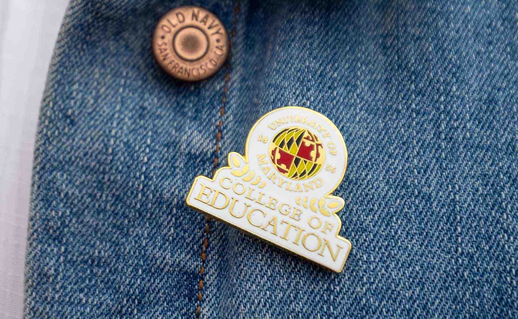 A pin that featured a globe and says University of Maryland College of Education, pinned on jean material