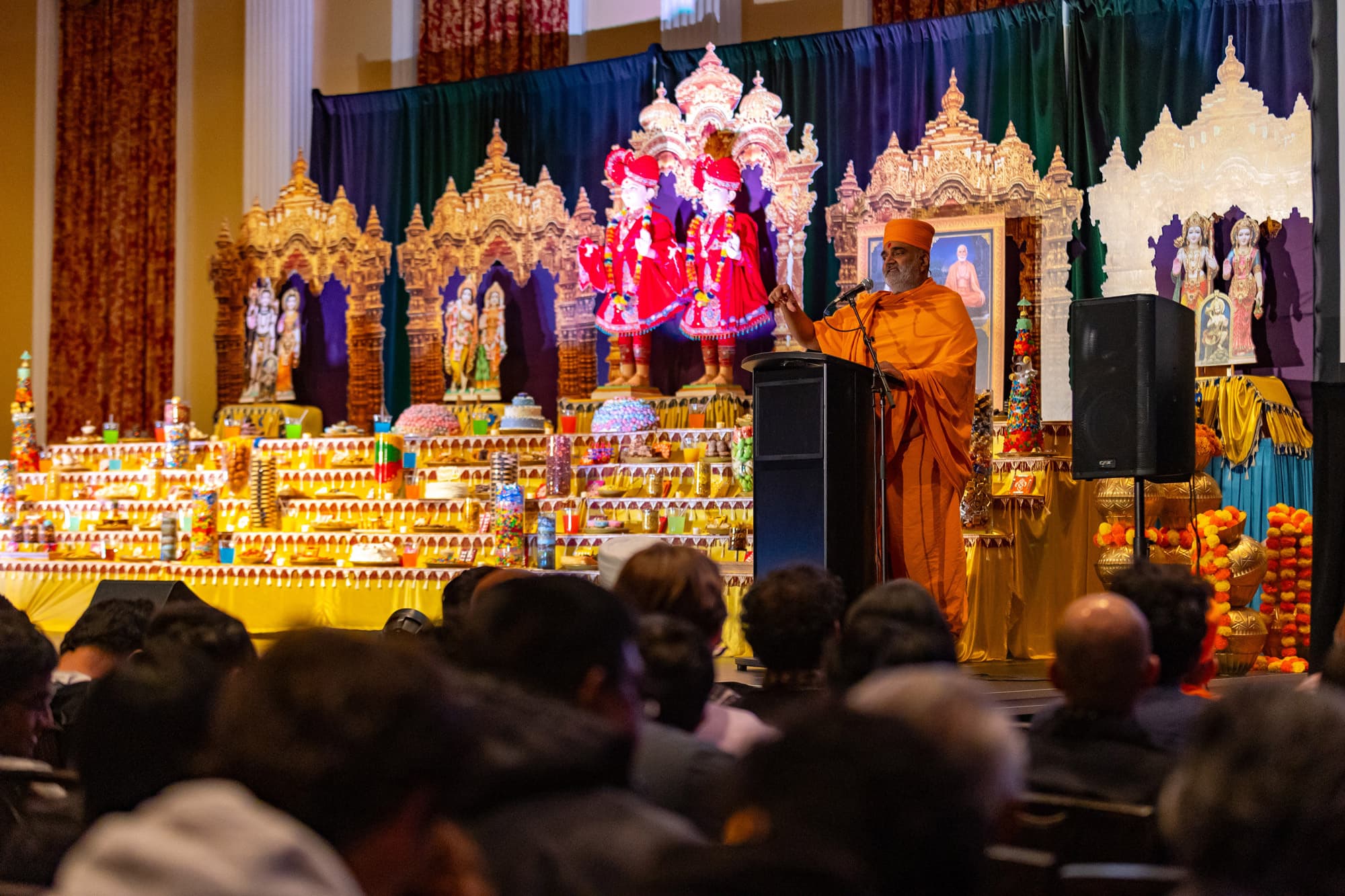 A Hindu priest speaks on stage in front of a colorful yellow display