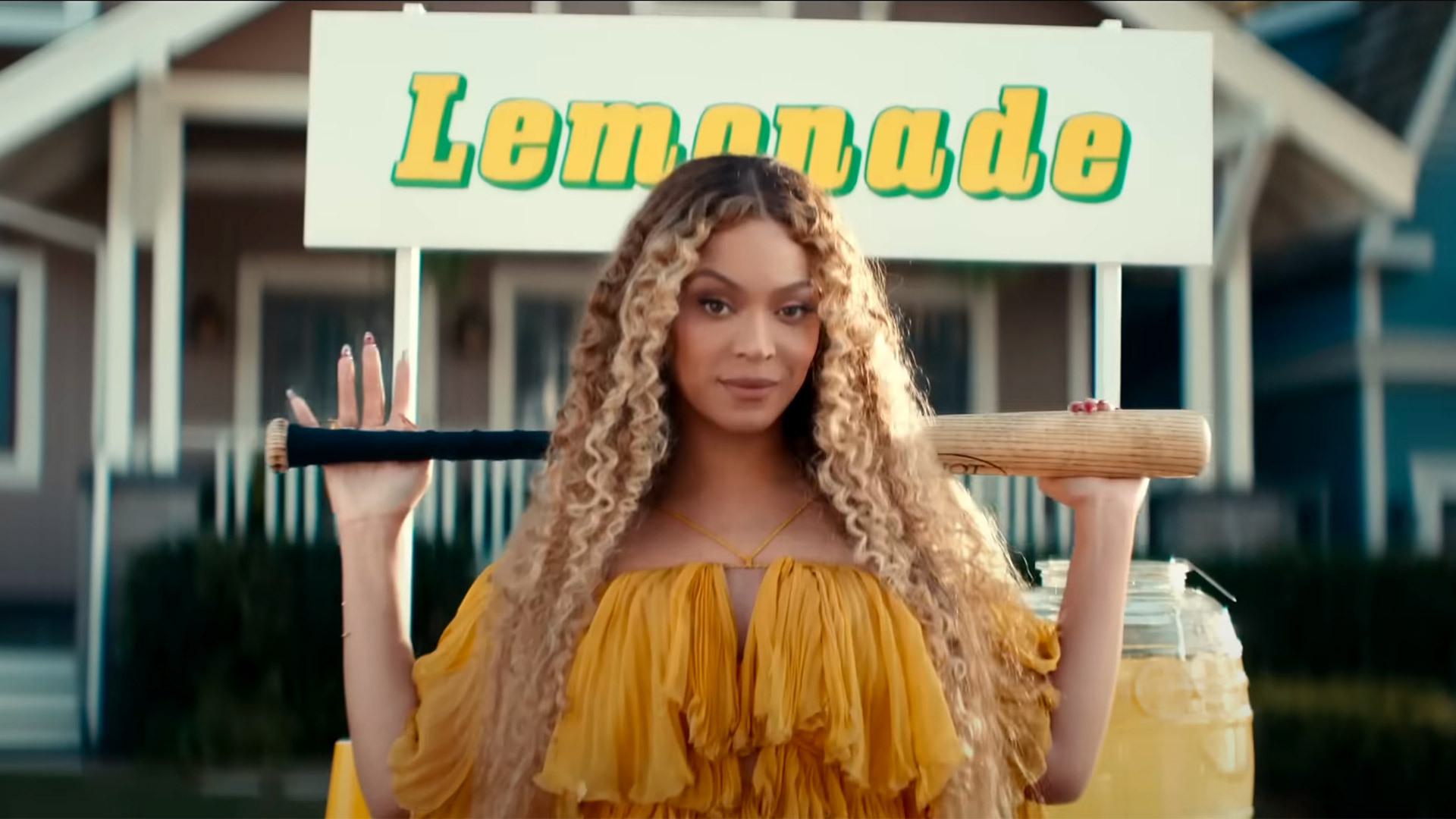 Beyonce carrying a bat behind her head in front of a sign that says Lemonade