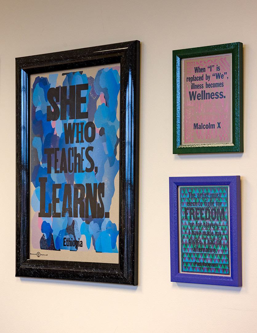 three wall prints that read, "She who teaches, learns," "When I is replaced by we, illness becomes wellness - Malcolm X," and "The artist must elect to fight for freedom or for slavery. I have made my choice. I had no alternative. - Paul Robeson"