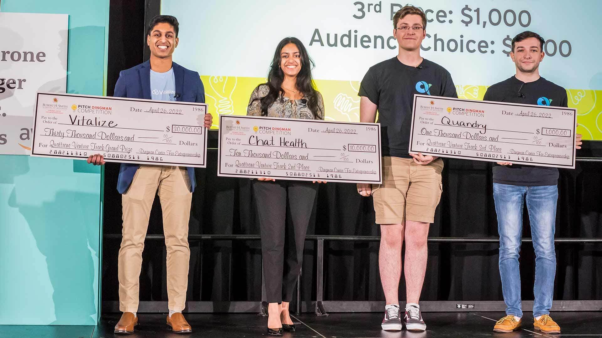 Four students hold three giant checks at Pitch Dingman Competition