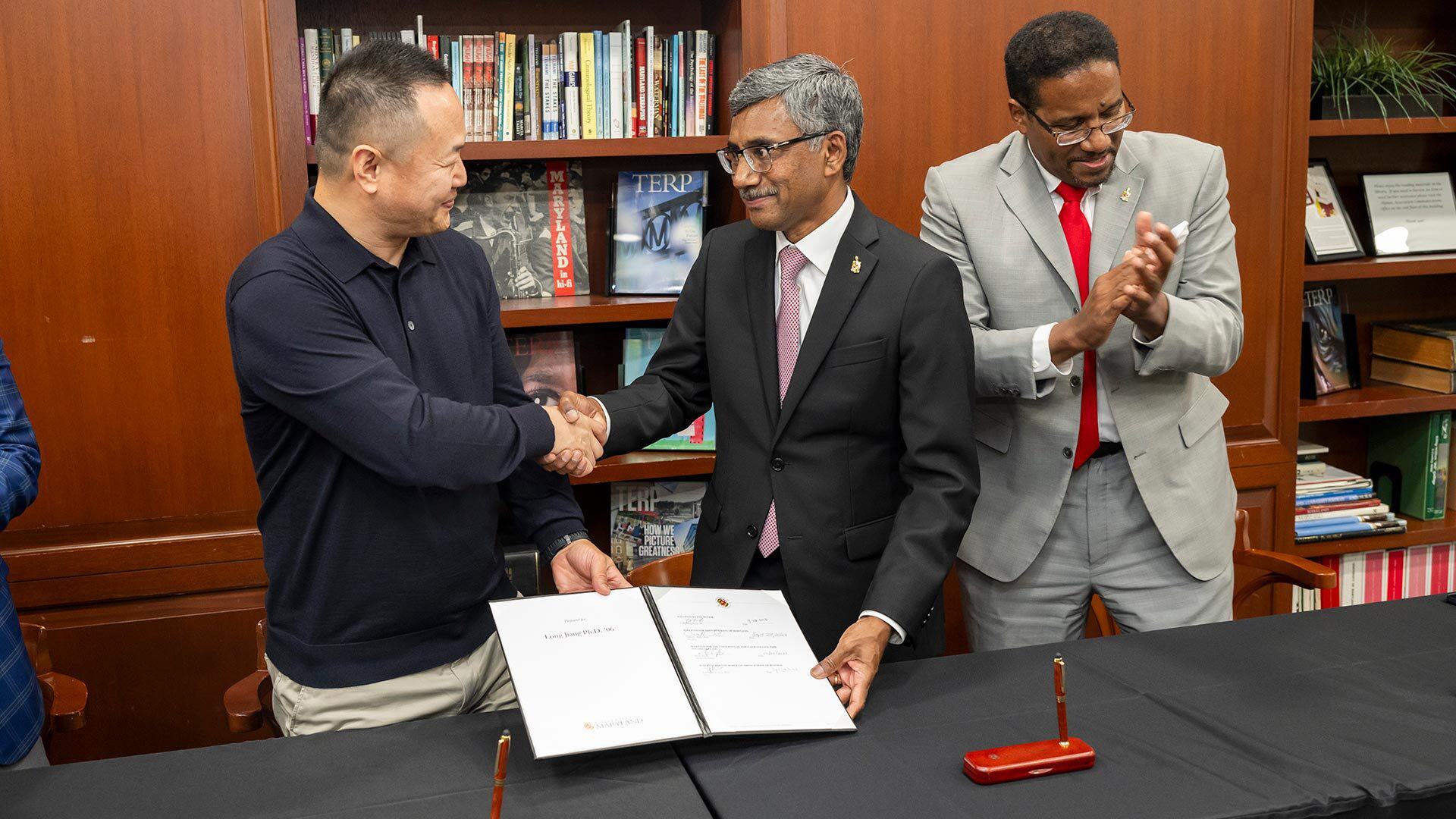Two men shake hands while another one claps