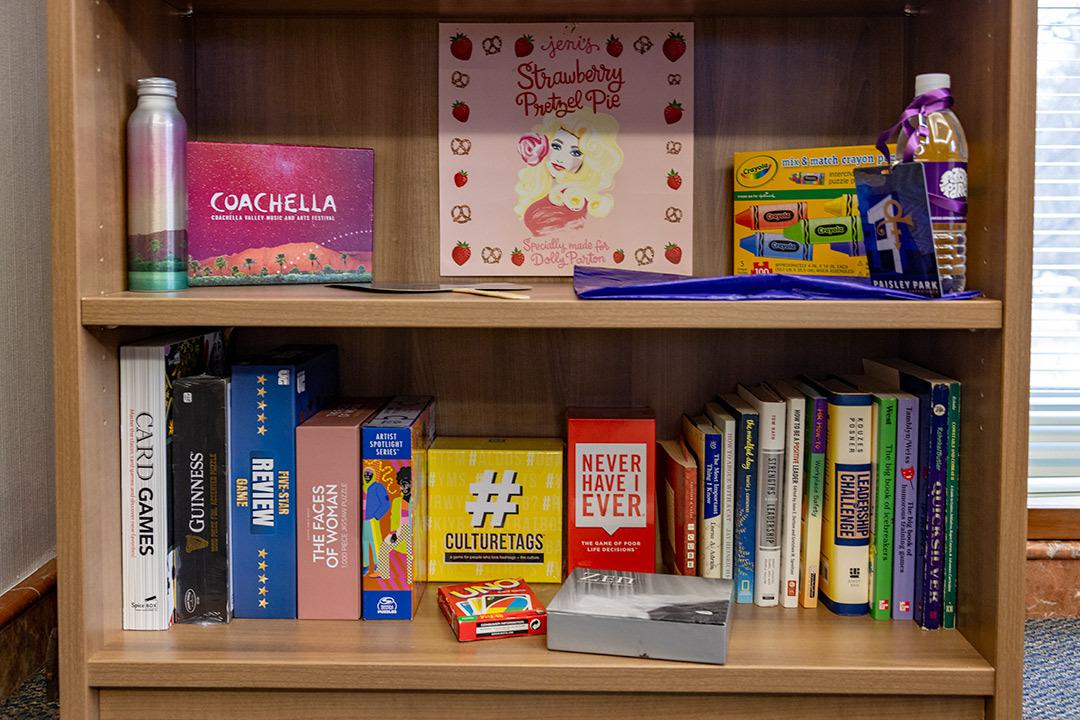 Bookshelf with Coachella, Dolly Partin and Paisley Park items on one shelf, games on bottom shelf