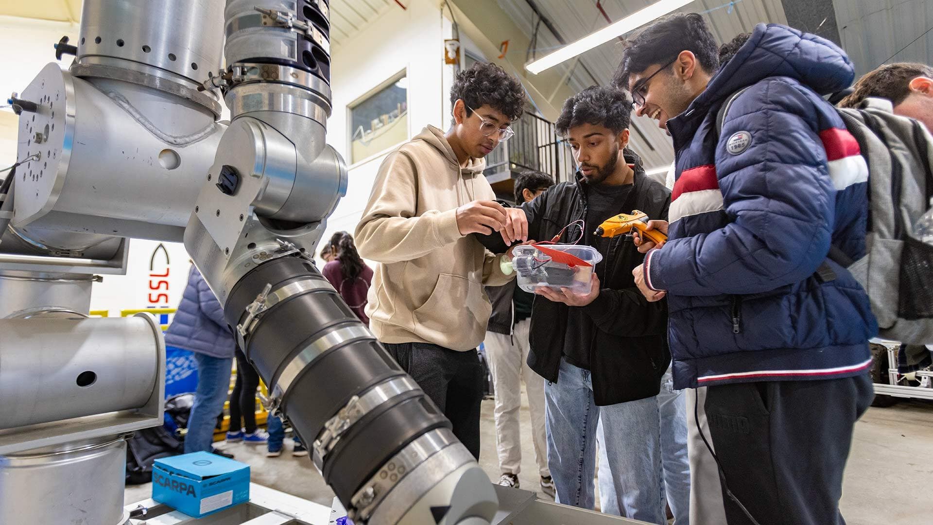 three students next to a robotic arm